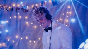 Person wearing headphones, smiling, with string lights in background.